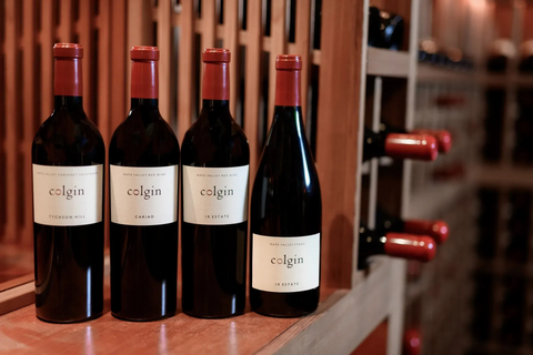 Four bottles of Colgin wine on a wooden shelf with a wine rack in the background.