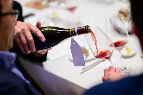 Person pouring red wine into a glass with a visible brand label.