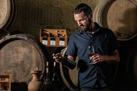 Man tasting wine in a cellar with barrels and bottles around
