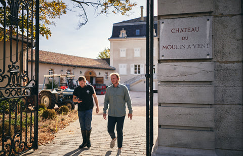 Two men walking towards a building with a sign reading 'Chateau du Moulin a Vent'.